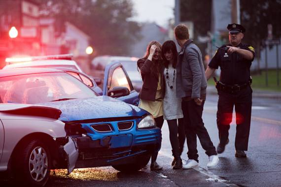 People standing near a damaged car after a collision while a police officer directs traffic